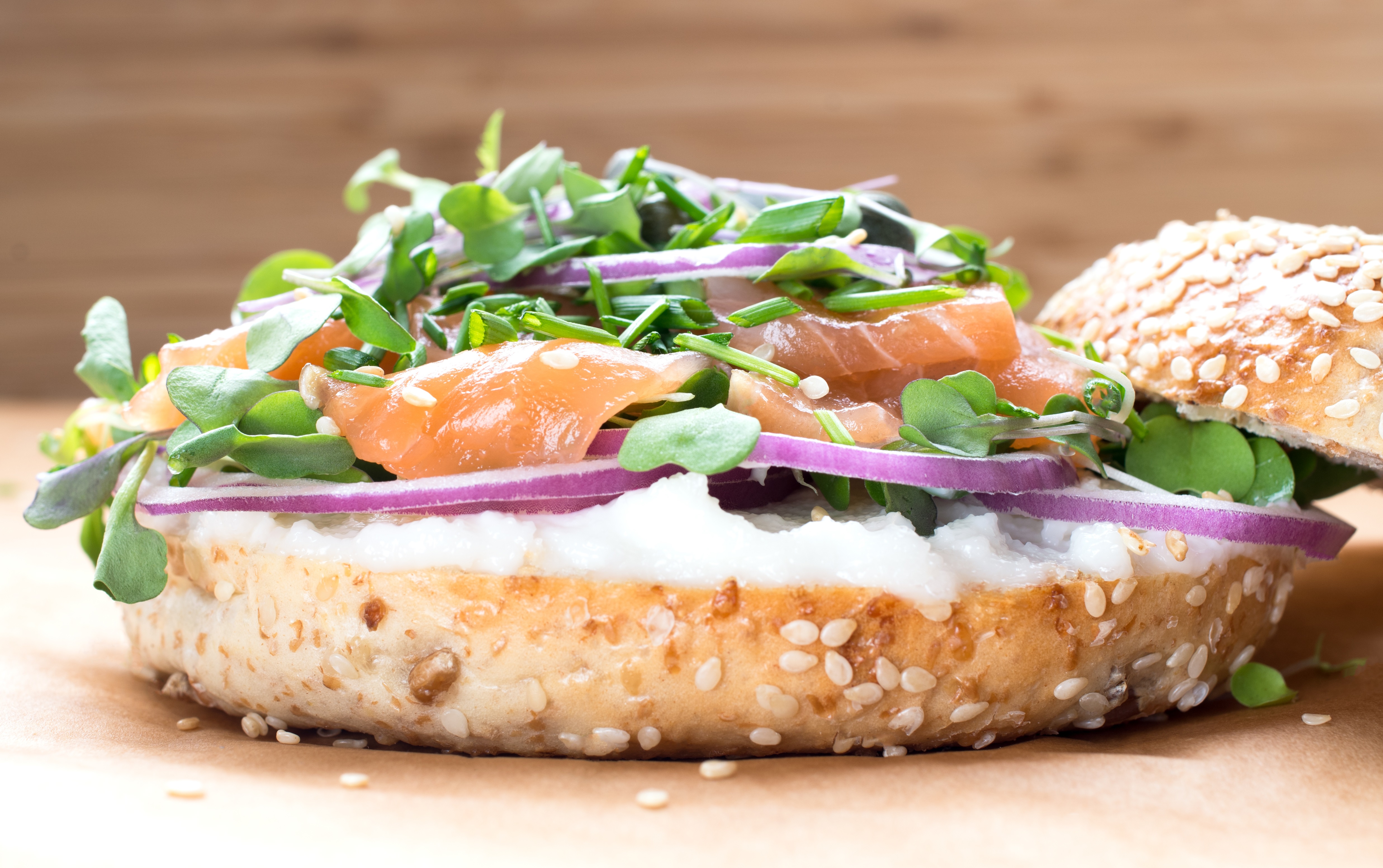Bagel sandwich with creame cheese, salmon,onion,tomato,greens,chives close-up on a wooden background. Delicious bagel, golden bake color, soft inside, crispy outside.